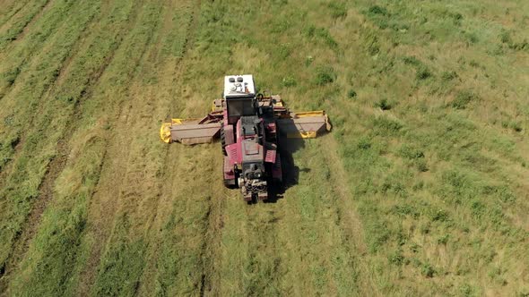 Aerial View of an Agricultural Machine Mowing Juicy Grass on a Sunny Day in a Meadow alt