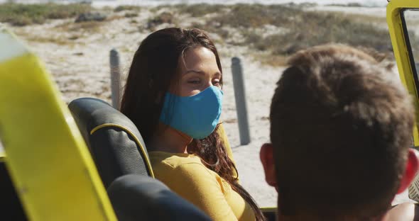 Happy caucasian couple wearing face masks sitting in beach buggy alt