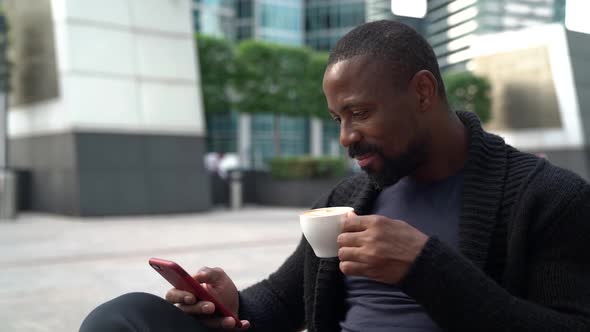Black Man Is Relaxing at Morning at Street Cafe, Drinking Coffee and Reading News at Internet alt