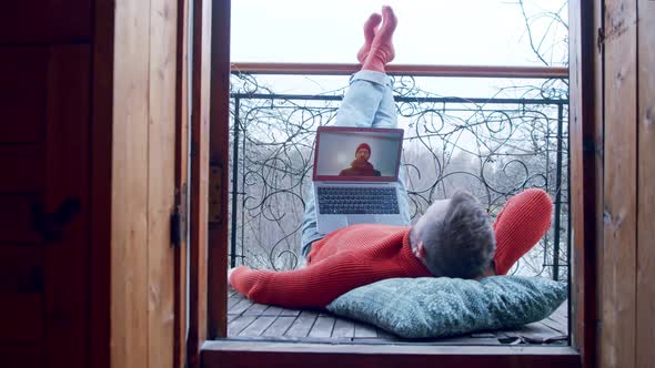 a Man on His Balcony Talks To a Friend or Work Colleague with His Legs Thrown Back and Relaxed alt
