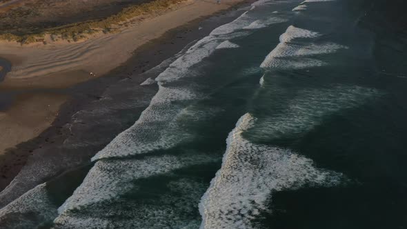 aerial view of low flat ocean waves crashing onto Morro Bay beach during sunset alt