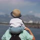Mom Carries Son on Shoulders Looking at Sea Near Mountains - VideoHive Item for Sale