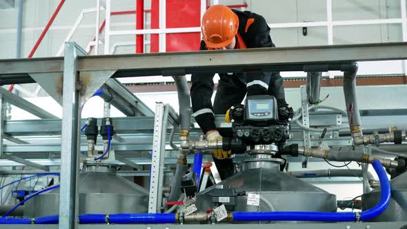 A Worker Wearing a Helmet and Gloves Removes the Pipes to the Distribution Unit to Control the alt