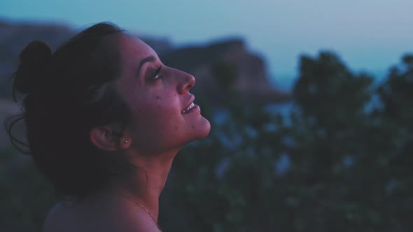 Closeup of a young woman on a red top smiling and touching the plants by the sea alt