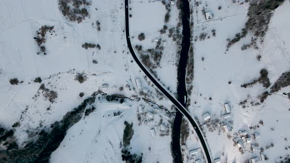 Aerial View of a Road Goes Through Snowy Village and Frozen River in Carpathian Mountains Winter