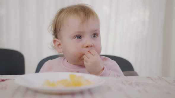Cute baby eating an orange next to a table alt