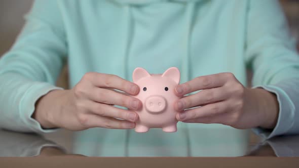 Female hands putting a piggy bank on the table. Money saving concept. alt