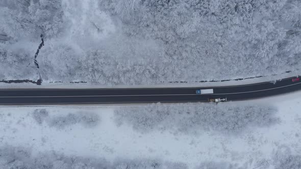 Aerial shot: a grader is cleaning the road of a snow in winter forest.