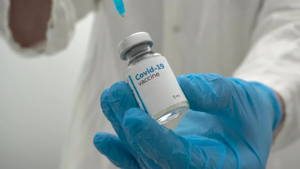 Close up of a doctor in medical blue gloves filling a syringe with a dose of coronavirus vaccine