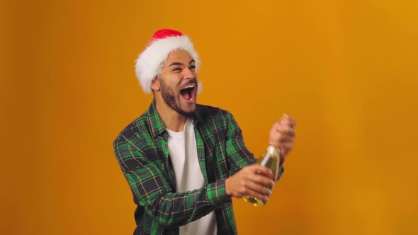 African American Man in Santa Hat Opening Champagne Bottle with Explosion Against Yellow Background alt