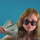 Girl in Glasses Waving Dollars on a Blue Background