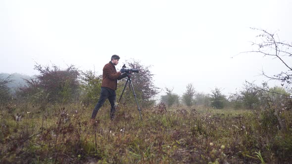 Wildlife photographer using DSLR camera on a tripod in a misty moor. alt