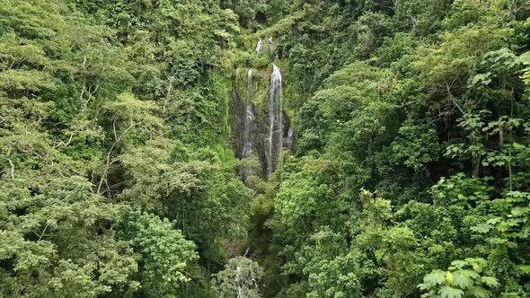DRONE AERIAL SHOT ZOOMING IN WATERFALL SURROUNDED BY TREES. alt