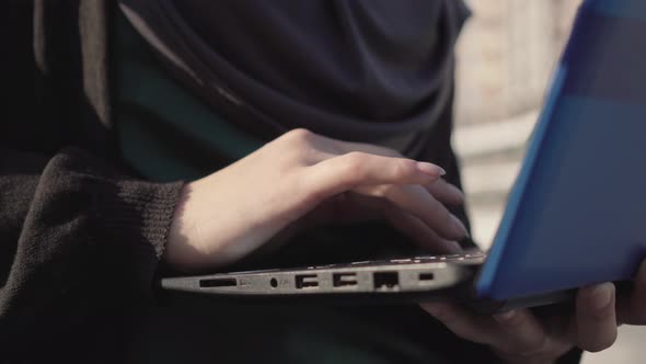 Close-up Hand of Muslim Woman in Traditional Clothes Typing Fast on Laptop Keyboard. Unrecognizable alt