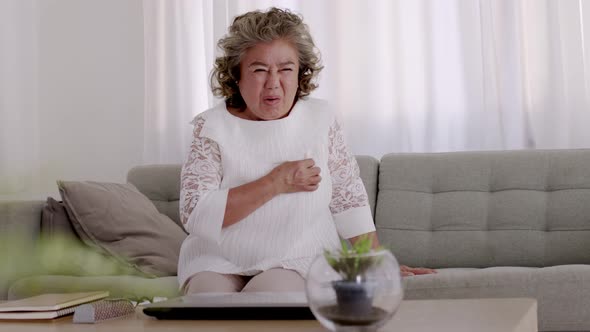 Asian Elderly woman Chest pain due to heart disease on the sofa in the living room. alt