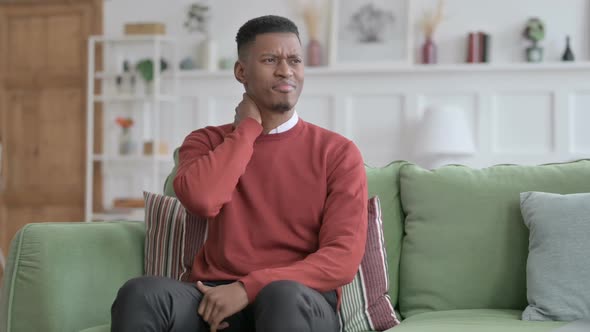 African Man having Neck Pain while Sitting on Sofa alt