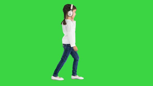 Little Girl Dressed in White Walking in Headphones and Nodding Her Head To the Music Beat on a Green alt
