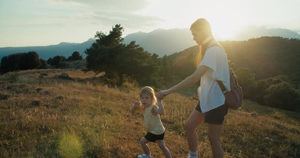 Woman Holding Child Hand and Climbing Mountain on Vacation Travel at Sunset alt