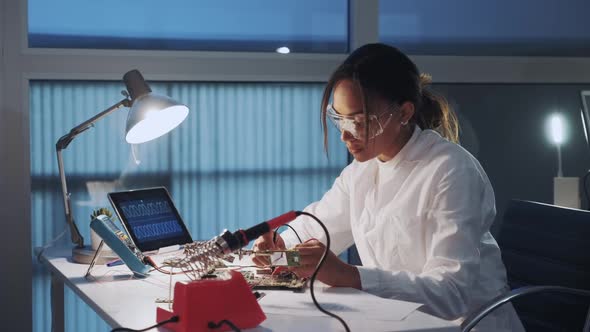 Middle Close Up of African American Electronics Engineer in Protective Glasses Checking Motherboard alt