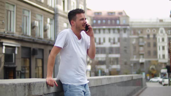 Handsome Young Man in a White Tshirt in the Center of the Old City Talking on a Smartphone alt