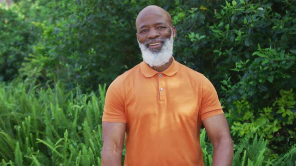 Portrait of african american senior man smiling and crossing his arms in the garden alt