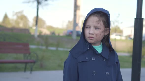 Portrait of a Sad Teenage Girl with a Burned Face Walking Down the Street with a Hood on the alt