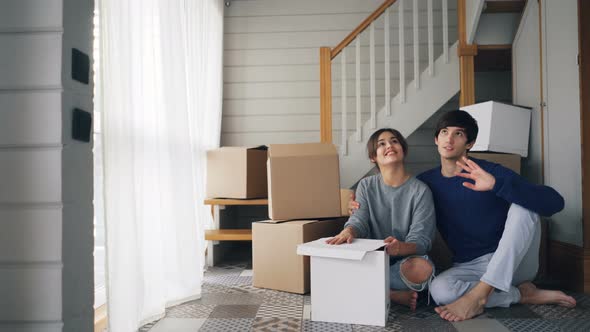 Young People Husband and Wife Are Talking and Kissing Sitting on Floor of New House Near Staircase alt