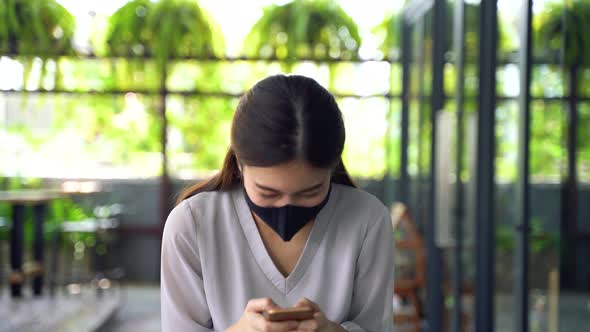Young Beautiful Asian Woman with Surgical Mask for Face Protection Using a Smartphone at Office alt