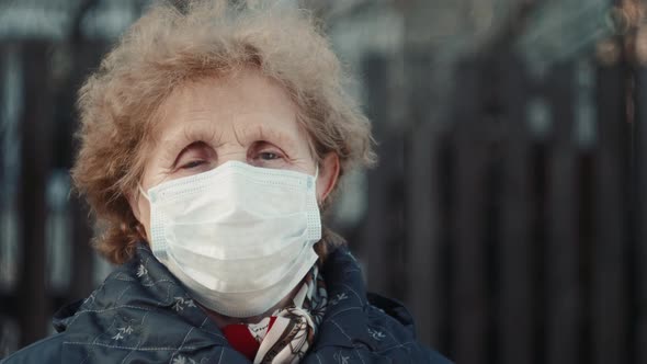 Elderly Woman in a Respirator Protection Mask is Walking the Street alt