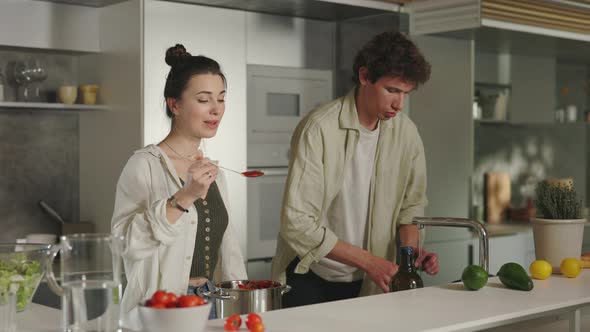 Woman Giving Tomato Sauce on Spoon for Husband to Try alt
