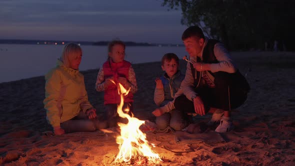 Happy Family Eating and Talking By Fire During Picnic on Night Beach