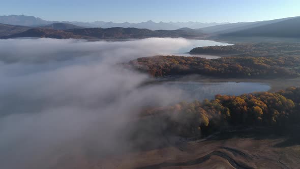 Drone Shot of a Fog Just Over the Lake Surrounded By Yellow Autumn Forest