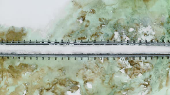 Person Walking In Narrow Bridge Over A Frozen River In Norway In Winter - aerial shot alt