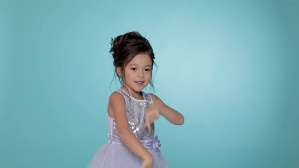 Beautiful Little Child Girl in Silver Dress Dancing on Blue Background.