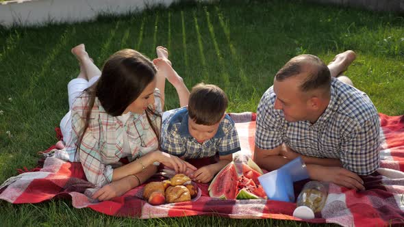 Happy Family Members Lie on Stomach on Red Blanket at Picnic alt
