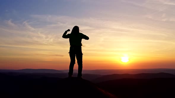 Silhouette of a Young Woman Dancing on a Mountain Top at Sunset