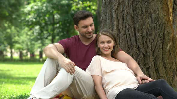 Pregnant Couple Sitting in Park, Smiling Into Camera, Happy Maternity, Parenting alt