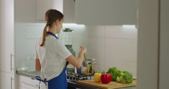 The Woman Is Taking a Wooden Spatula and Mixing Boiling Dishes at Pan on the Stove