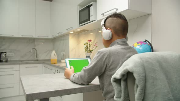Moving Shot of Preteen Black Boy in Headphones Using Tablet at Home alt