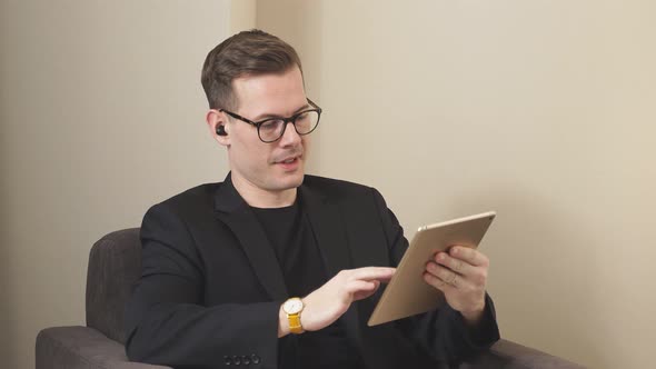 Male in Elegant Suit Sit on Couch Working on Digital Tabletwearing Wireless Headphones