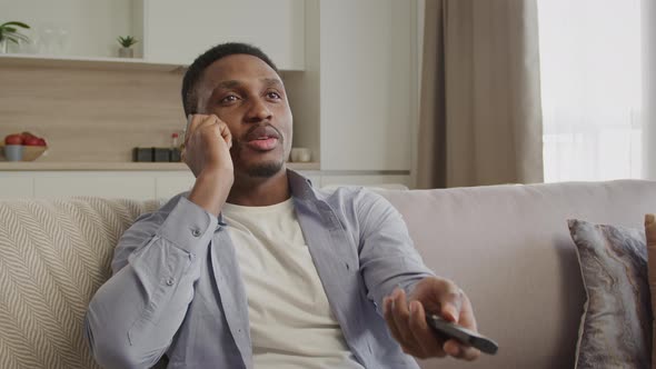 Young African American Man Having a Conversation with Cable Network Support and Using His Tv Remote alt