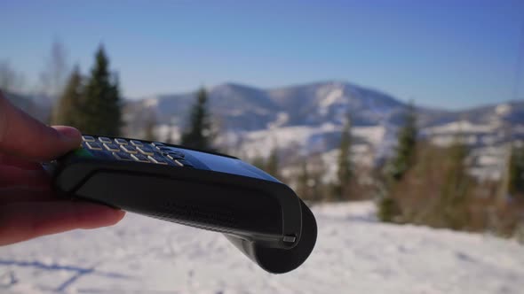 Female Hand Paying with Mobile Phone and Contactless Terminal on Ski Resort alt