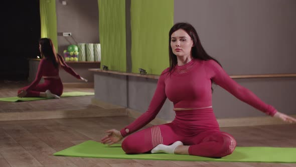 Fitness Training  Young Woman in Pink Costume Sitting on the Yoga Mat and Leaning to the Sides alt