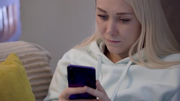 Young female customer using mobile phone while sitting on sofa at home. alt