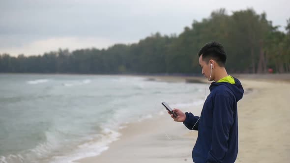 Handsome man running using smartphone on the beach, Asian man running on the beach.