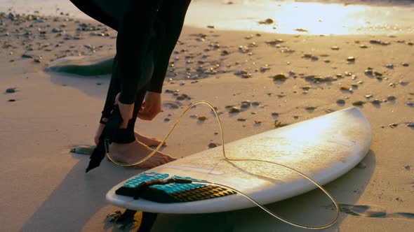 Side view of mid-adult caucasian male surfer tying surfboard leash at the beach 4k alt