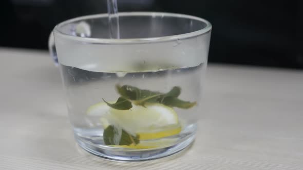 Water is Poured Into a Glass with Lemon and Mint