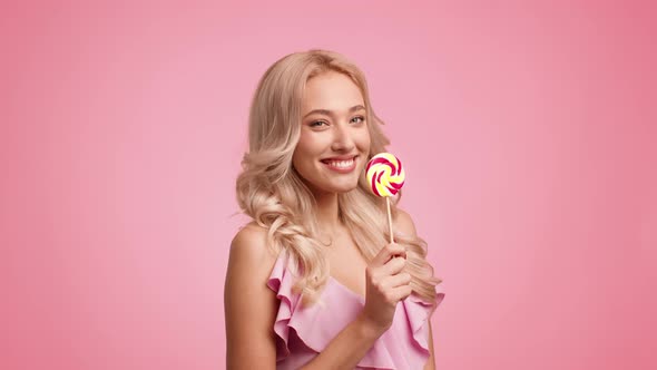 Woman Posing Eating Lollipop Kissing Candy Winking Eye Pink Background alt