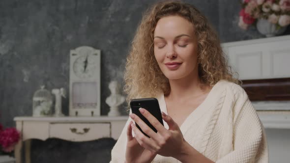 Handheld Shot of a Curly Caucasian Woman Texting on Her Smart Phone Indoor alt