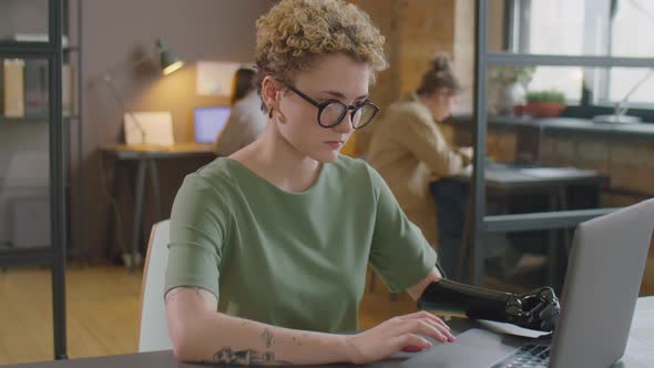 Woman with Prosthetic Arm Working on Laptop in Office alt